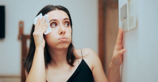 sweating woman checking her thermostat